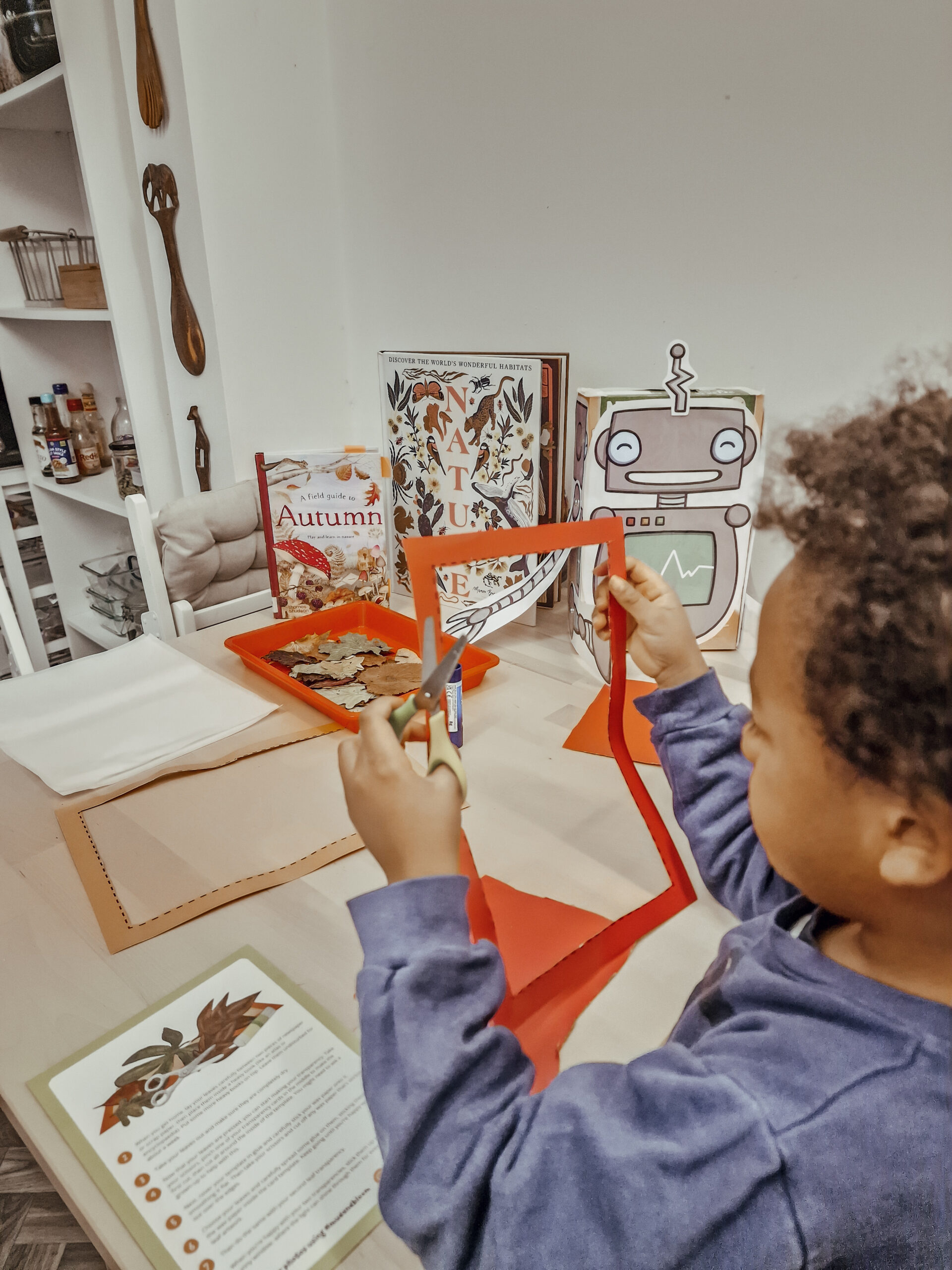 Boy cutting out a frame using red card and autumn books in the background