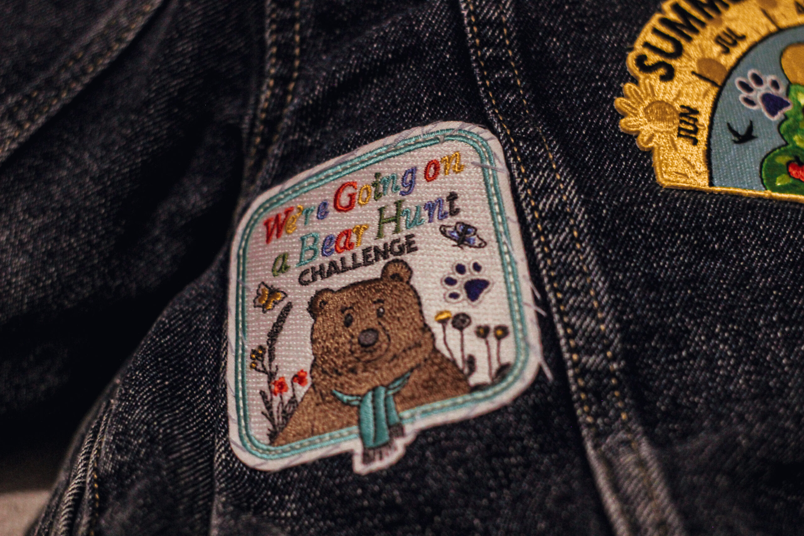 A Denim Jacket With a Square Goingon A Bear Hunt Badge Sewn On It.